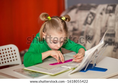 little pretty girl with poor posture, slouching, 7-8 years old, first grader, at her desk, doing homework, teaching lessons, drawing on the line Royalty-Free Stock Photo #1618055422