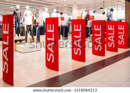 Red billboards stand at the entrance to a clothing boutique with sale information. In the background are manikins and hangers. Promotion, advertising, shopping and black friday concept