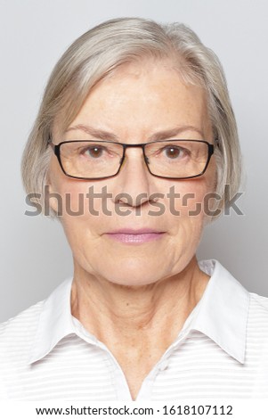 Biometric passport photo of a senior woman with glasses, neutral gray background.