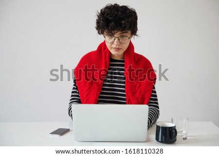 Serious young dark haired curly woman with short trendy haircut wearing eyeglasses while working over white background with modern laptop, looking at screen with concentrated face