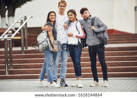 Posing for a camera. Group of young students in casual clothes near university at daytime.