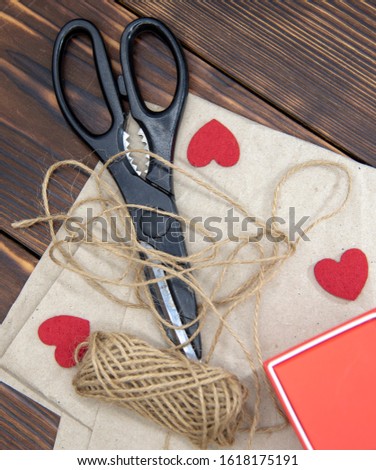 Scissors, coarse thread, and a gift box lie on Kraft paper on a dark wooden background.