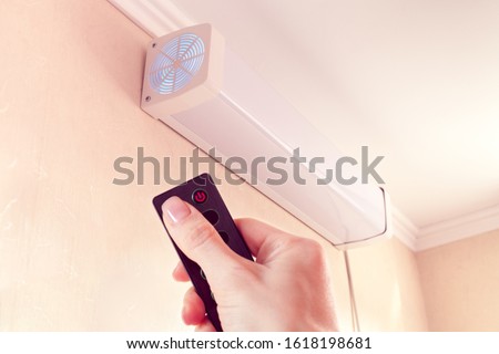 hand from remote-controlled includes bactericidal air recirculator hanging on wall for quartzing air in room Royalty-Free Stock Photo #1618198681