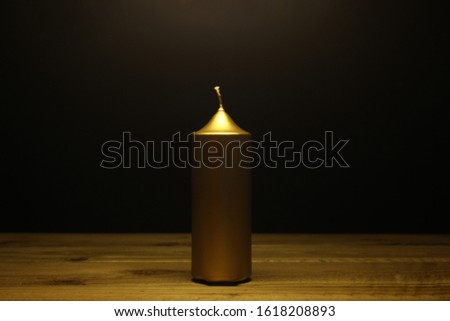 golden candle with no flame rest on a wooden table with black background and copy space for your text