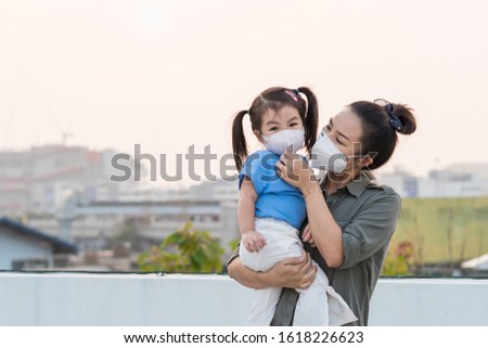 Asian mother and little young daughter wearing mask for prevent dusk pm 2.5 bad air pollution on deck in Bangkok city Thailand 2020.  Royalty-Free Stock Photo #1618226623