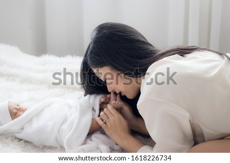 Portrait of asian mother playing with newborn baby, baby talking to mother. mother is kissing feet on the baby, Health care family love together. Asian girl lifestyle. Asia mother's day concept, Mom's