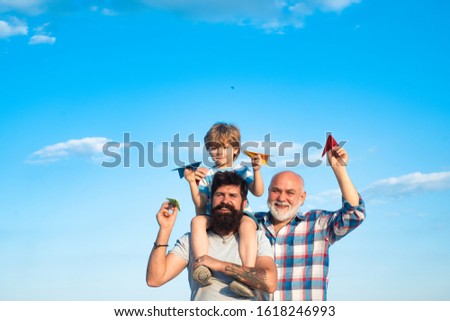 Happy grandfather father and grandson with toy paper airplane over blue sky and clouds background. Happy men loving family. Father son and grandfather relaxing together