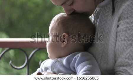 
Candid mother kissing baby infant son casual authentic moment by window