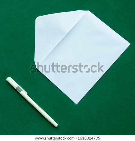 Traditional white letter envelope with ballpoint pen next to it, on a green background