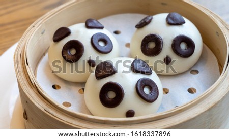A picture of 3 Chinese steamed buns in the shape of cute, adorable pandas in the wooden basket. It was pictured in a bright and soft tone. It can also be called Baozi in the local Chinese language.