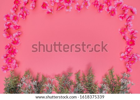 a lot of artificial pink flowers put around a picture and artificial green plants on the bottom. those are placed on a pink background