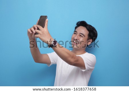 Portrait of young Asian man smiling while taking selfie photograph of himself on his smart phone