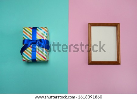 The concept of birthday. Gift box with ribbons and a bow and a wooden photo frame on a pink and light blue background.