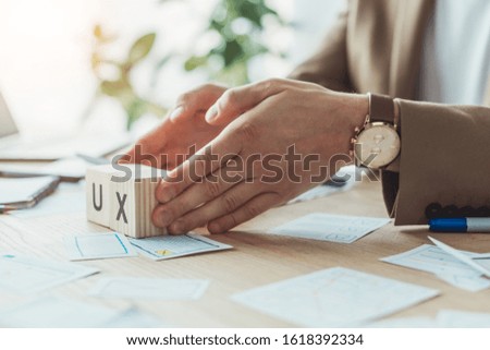 Cropped view of designer holding wooden cubes with ux letters beside app sketches on table