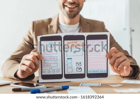 Cropped view of smiling designer showing mobile website wireframe sketches at table