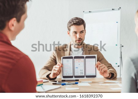 Selective focus of designer showing layout of mobile web prototype to colleagues in office