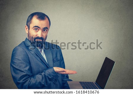 Closeup portrait of mature middle age business man showing pointing presenting a laptop screen with an open palm. Mixed race bearded model isolated on gray studio wall background with copy space.