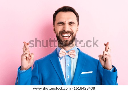bearded man in suit with crossed fingers on pink