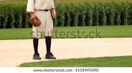 Baseball player in old baseball uniform and baseball glove, on the playing field.  Corn in the background.   Royalty-Free Stock Photo #1618495090