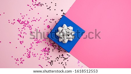 closed square blue gift box with silver bow on a pink background, near multi-colored sequins, top view, festive backdrop