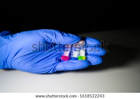 Scientist holding Three colourful liquid in different LCMS glass vial on a white bench with black background for medical research in a chemistry laboratory 