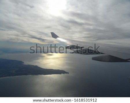 landscape with airplane wing and sky with clouds and seascape with sun flare
