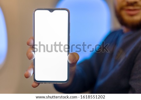 Mockup smartphone airplane. Young attractive european man holding blank screen smartphone in hands in airplane. Mock up for a game, mobile application, web site a horizontal oriental. Stock photo.