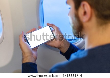 Mockup smartphone airplane. Young attractive european man holding blank screen smartphone in hands in airplane. Mock up for a game, mobile application, web site a horizontal oriental. Stock photo.