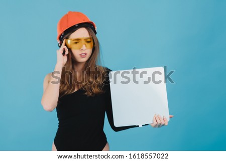 beautiful girl in yellow glasses and a protective helmet holds a white board in her hand on a blue background