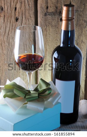 Red wine glass and bottle with gift on wooden background