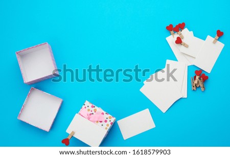 open square cardboard empty box and white blank paper rectangular business cards on decorative clothespins, item lies on a blue background, top view, copy space