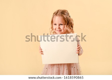Cute curly girl of four years old. laughs emotionally. In a smart pink dress Girl holding white blank paper vertically. Leaflet presentation. Pamphlet hold hands. Woman show clear offset paper.