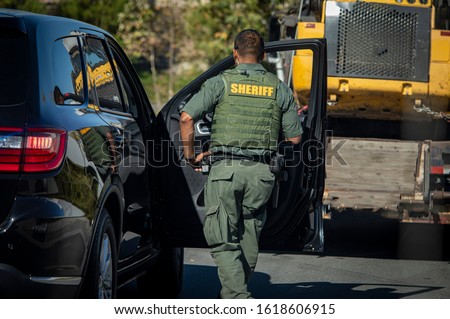 Behind view of police officer in bullut proof vest looking into passanger side of car at the scene of an accident Royalty-Free Stock Photo #1618606915
