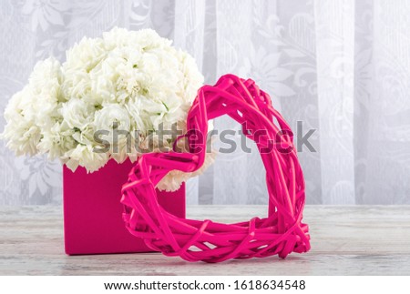 A bouquet of white roses in a pink box and a pink picture frame rattan heart, close-up. Valentine's day, wedding, declaration of love. Space for text, front view, copy space.