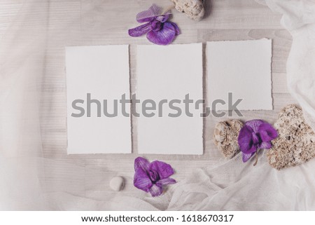 Feminine wedding, birthday mockup scene, baby shower card, presentation. Watercolor textured paper greeting cards, stones, orchidea flowers. White textile on a table background. Flat lay, top view