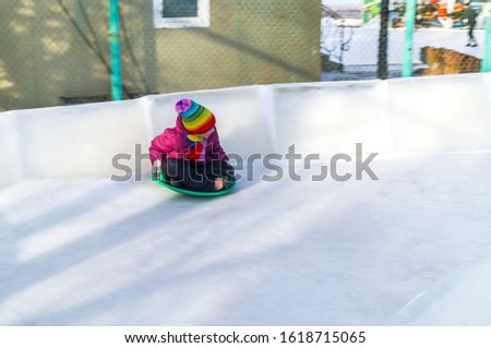 Child rolls down an ice slide. Merry winter sport family. Bright clothes rainbow hat.