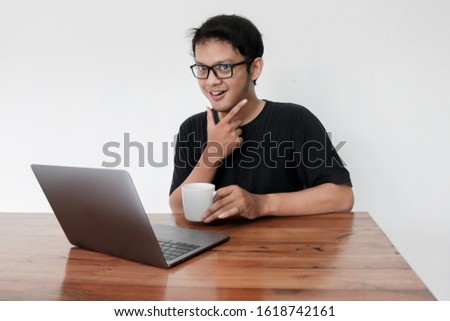 Smile face and Funny tricky awkward smirk face of Young Asian man with hand in chin in a black t-shirt in a front of a laptop.
