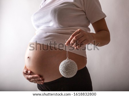 Pregnant woman smiling, touching her belly, standing over white wall. Copy space. Christmas, New year concept.