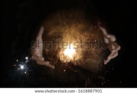 sparkles between female hands trying to capture the light as if a magician in a dark black background, few sparkles flying away in background Royalty-Free Stock Photo #1618887901