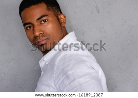 Close-up portrait of a serious handsome young african-american dressed in a white shirt posing on a gray bokeh background. Concept of confident successful young businessman. Advertising space