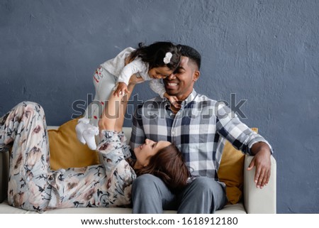 Charming young loving mixed race couple enjoy chatting with their little african american daughter sitting on a cozy sofa in the room. Concept of a family from different countries. Copyspace