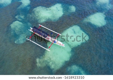 View from above, stunning aerial view of a Jukung canoe sailing on a beautiful turquoise sea in Nusa Penida, Indonesia. A Jukung is a small wooden Indonesian outrigger canoe.
