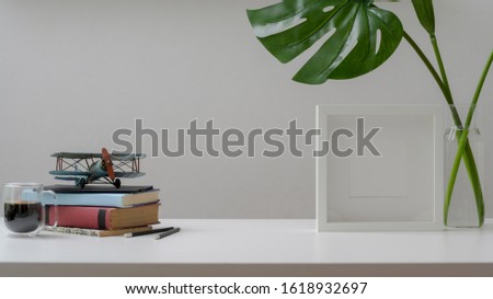 Close up view of minimal workspace with copy space, books, mock up frame and decorations on white wooden desk with white wall background 