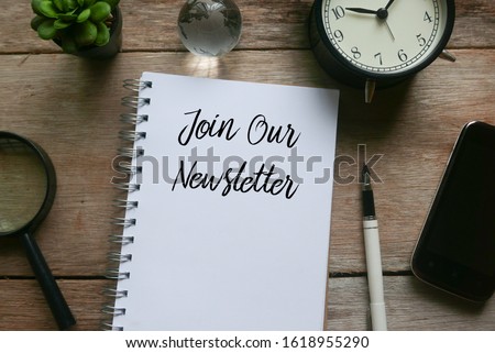 Top view of magnifying glass,plant.glass globe,clock,mobile phone,pen and notebook written with Join Our Newsletter on wooden background.