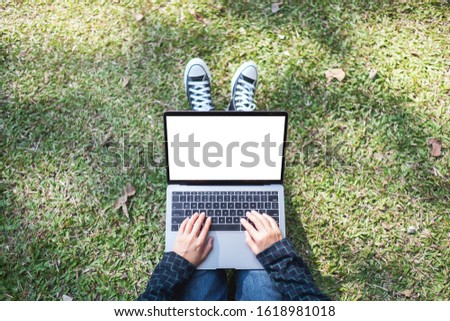 Top view mockup image of a woman using and typing on laptop with blank white screen while sitting in the outdoors