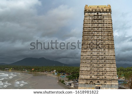 Beautiful view of magnificent 20-storeyed Gopuram tower of Lord Shiva Temple in Murdeshwara with mountains, forest and calm sea waves in background during rainy season. Medieval Dravidian architecture Royalty-Free Stock Photo #1618981822