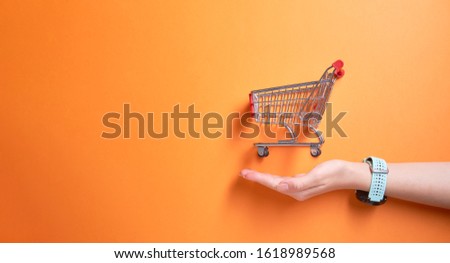 Iron small trolley from supermarket onempty orange background in studio and mans palm. Royalty-Free Stock Photo #1618989568