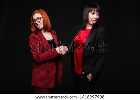 Businesswomen showing disgust while shaking hands.Business partners showing dislike to their business deal. Isolate on black.