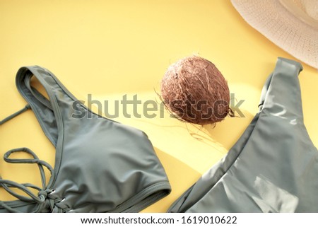 Khaki swimsuit, coconut and straw hat on a yellow background. Summer picture.  Top view. Copy space.