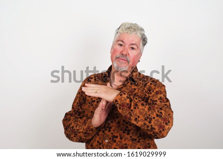 Middle aged caucasian man tired and bored, making a timeout gesture, needs to stop because of work stress, time concept. Standing against gray wall.